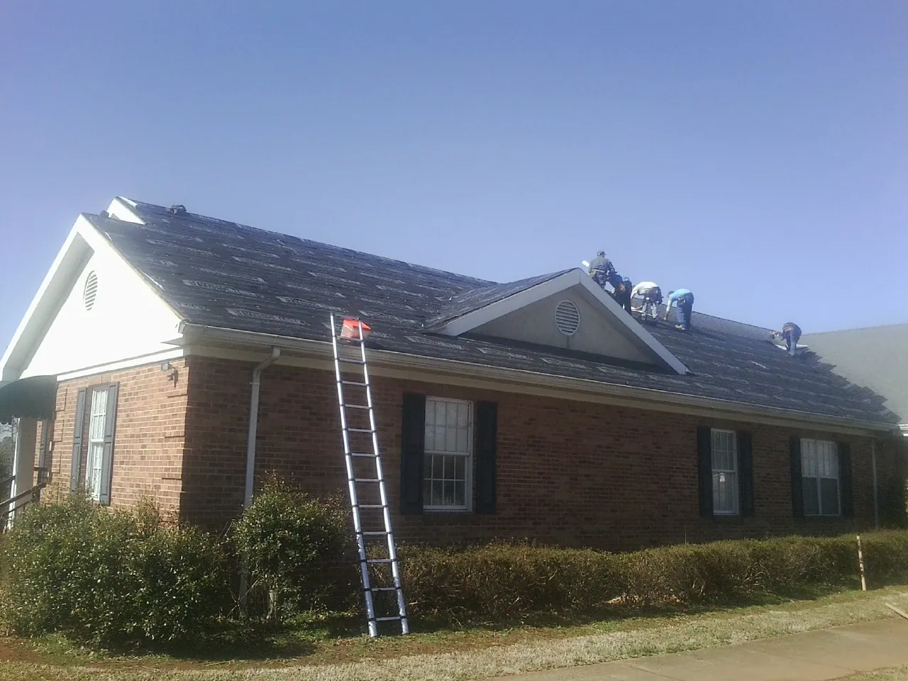 Crew tearing shingles off a brick ranch roof with a ladder set — Emergency Roof Repair work by our crew in Sebastian