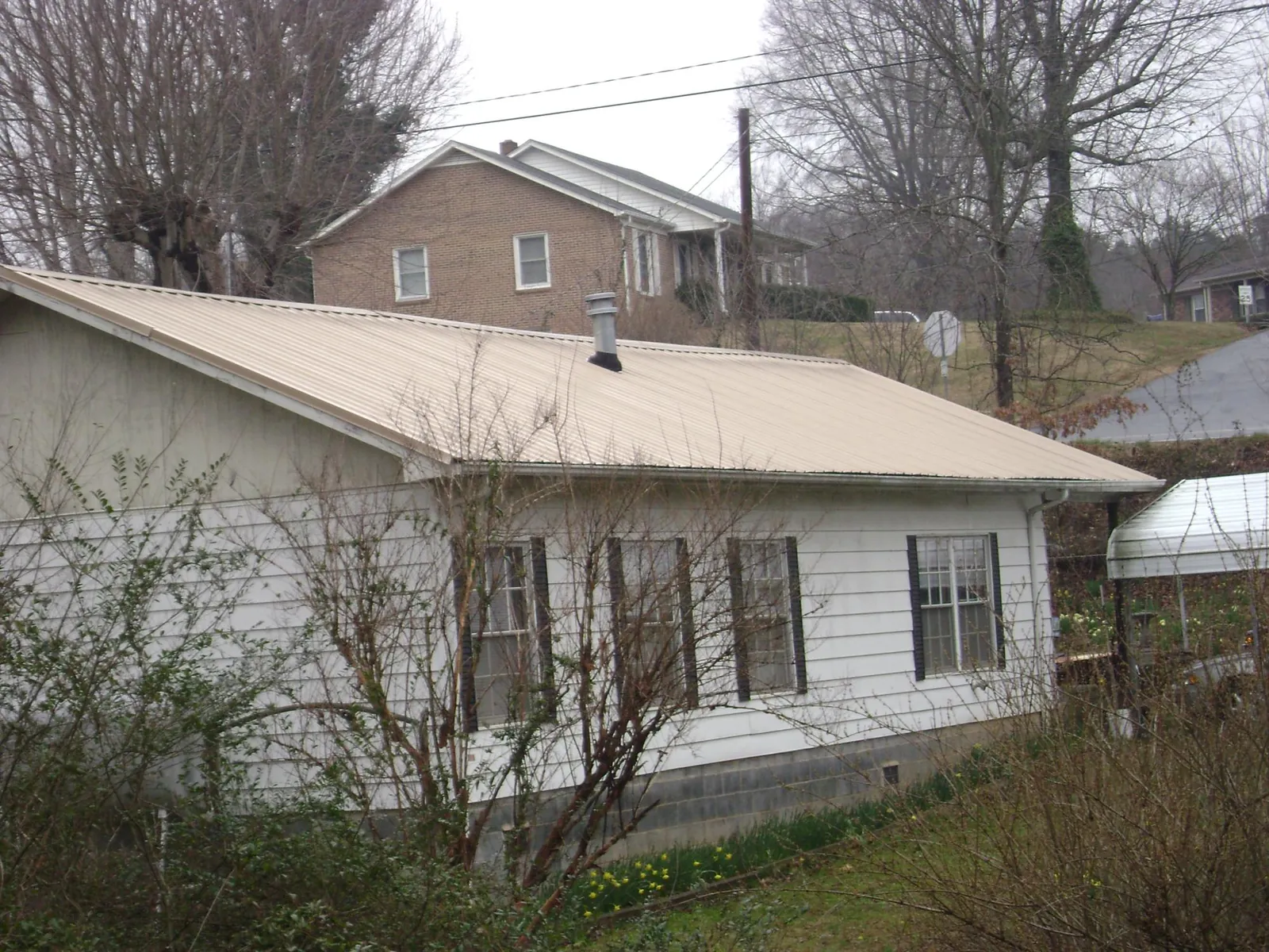 Tan metal roof on a white sided house set into a hillside — Commercial Roofing by Roofing Brothers in Sebastian