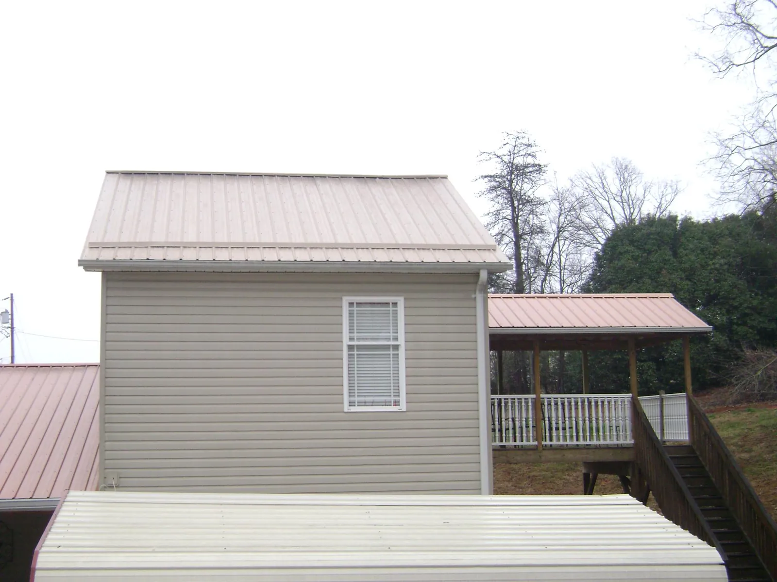 Tan metal roofs on a two story addition and attached porch, from a Roof Replacement job in Sebastian